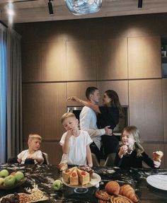 a group of people sitting around a table with cakes and fruit on top of it