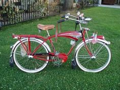 a red bicycle parked on top of a lush green grass covered field next to a fence