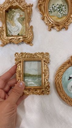 a person is holding up three pictures in gold frames on a white table cloth with flowers