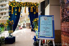 an entrance to a building decorated with flowers and blue drapes, along with a welcome sign