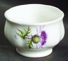 a white bowl with purple flowers painted on the outside and inside, sitting on a black surface