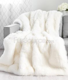 a white fur blanket sitting on top of a couch next to a vase with flowers