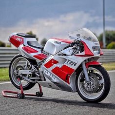 a red and white yamaha motorcycle parked on the side of a road with grass in the background