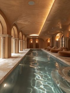 an indoor swimming pool in a large building with arches and columns on the ceiling, along with lounge chairs