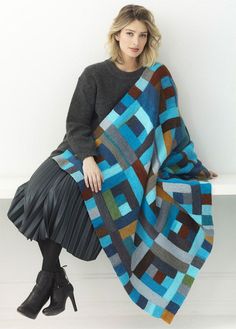 a woman sitting on a bench wearing a multicolored blanket