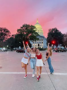 three girls standing in front of the capital building at sunset with their arms up and hands raised