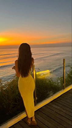 a woman in yellow dress looking out over the ocean at sunset with her back to the camera