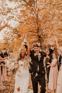 a newly married couple walking through the leaves with their hands in the air and throwing confetti