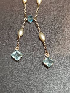 A 9ct gold  fresh water pearl, and blue crystal necklace. The necklace is not Hallmarked, but is stamped "375." 16 inch (406mm) chain, with two 1 inch (25mm) dangling pendants. The chain contains four crystals, and four grey shade fresh water pearls. It is joined at the bottom by a further blue crystal. Then suspended from the the centre in two strands is a further pearl, and a larger 5.5 x 5.5mm square cut blue crystal. The necklace is secured via a bolt ring clasp. Blue Crystal Necklace, Bolt Ring, Fresh Water Pearls, Fresh Water Pearl, Water Pearls, Square Cut, Blue Crystals, Crystal Necklace, Fresh Water