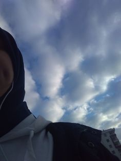 a person wearing a hoodie looking up into the sky with clouds in the background