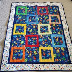 a blue quilt with colorful squares and dots on the bottom is laying on top of a bed