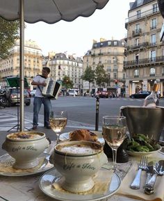 a table with food and wine on it in the middle of a city street, next to a man playing an accordion