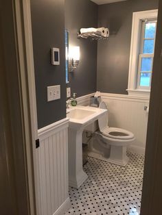 a white toilet sitting next to a sink in a bathroom under a window on top of a tiled floor