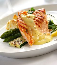 a white plate topped with fish and asparagus next to a glass of wine