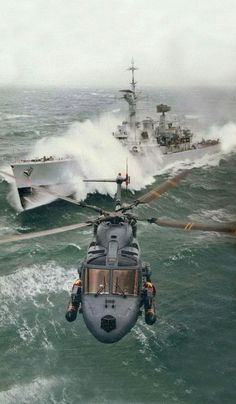 a helicopter flying over the ocean next to a large ship in the middle of the water