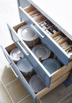 an open cabinet filled with dishes and silverware on top of a tiled countertop