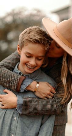 a woman is hugging a young boy who has his arm around her chest and wearing a hat