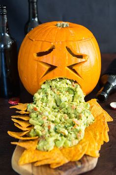 a carved pumpkin sitting on top of a wooden table next to some chips and bottles