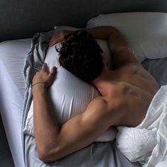 a shirtless man laying in bed with his head on the pillow and arms behind him