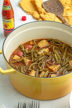 a yellow pot filled with green beans and tofu next to a bottle of hot sauce