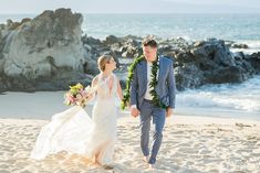 a bride and groom walking on the beach with leis around their necks holding hands