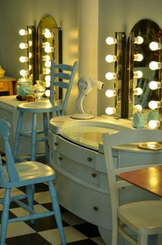 a vanity with stools and lighted mirrors in a room that has checkered flooring