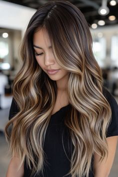 Woman with long, wavy, brown hair with blonde highlights looking down in a modern salon. Brunette Hair With Blonde Highlights Long Layers, Fall Blonde Brunette Hair Color, Brown Long Hair With Highlights, Caramel Highlights For Dark Brown Hair, Fall Dark Blonde Hair, Caramel Balayage On Dark Brown Hair, Fall Hair Highlights For Brunettes, Fall Hair Color For Brunettes Balayage, Chocolate Hair Color With Highlights