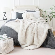 a white and grey bed with pillows and blankets on it, next to a plant