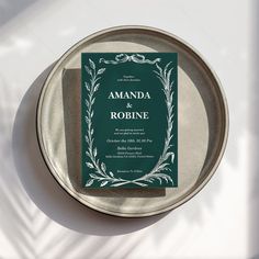 a green and white wedding card sitting on top of a silver plate next to a cup