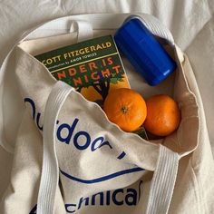 two oranges and a book in a tote bag