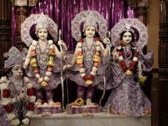 three statues of hindu deities are displayed in front of a purple curtained wall with red and white decorations