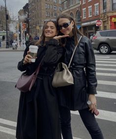 two women standing next to each other in the street with their arms around each other