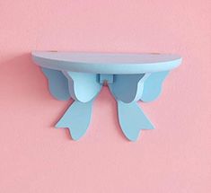 a blue shelf on a pink wall with an angel wing decoration hanging from it's side