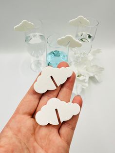 a hand holding two white paper clouds in front of some glass vases and flowers