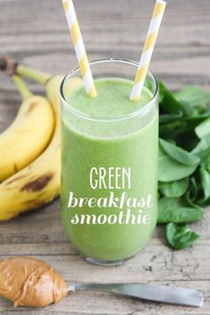 green breakfast smoothie in a glass with two straws on the table next to bananas and spinach leaves