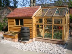 a small wooden building with windows and a barrel in the yard next to graveled area