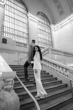 a man and woman walking up the stairs in an old train station, black and white photo