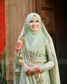 a woman in a green dress and headpiece smiles at the camera while standing outside