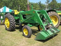 two large green tractors parked next to each other on top of a grass covered field