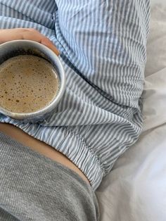 a person laying in bed holding a cup of coffee with both hands on their stomach