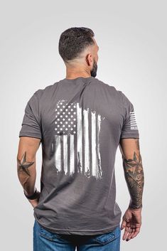 a man wearing an american flag t - shirt with tattoos on his arms and shoulder