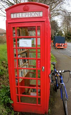 a bicycle parked next to a red phone booth with books on it's shelves