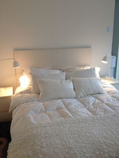 a bed with white sheets and pillows in a bedroom next to two lamps on either side of the bed