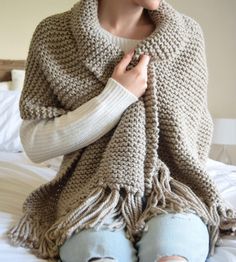 a woman sitting on top of a bed wearing a crocheted shawl