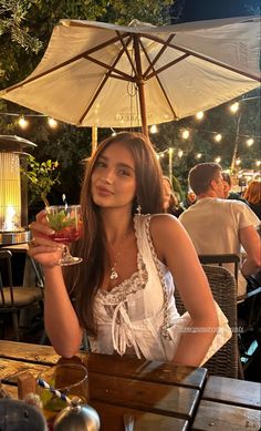 a woman sitting at a table holding up a drink in her hand and an umbrella over her head