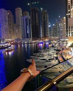 a person's hand pointing at boats in the water near a cityscape