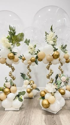 some white and gold balloons are in the air with greenery on them as well as flowers