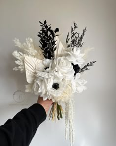 a person holding a bouquet of white flowers in their left hand, against a wall