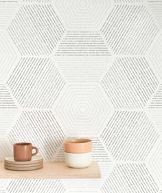 two cups are sitting on a shelf in front of a wallpapered background with hexagonal shapes