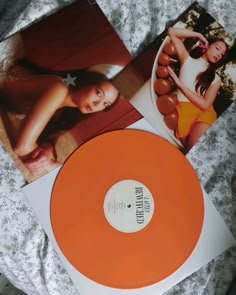 an orange vinyl record sitting on top of a bed next to two other pictures and papers